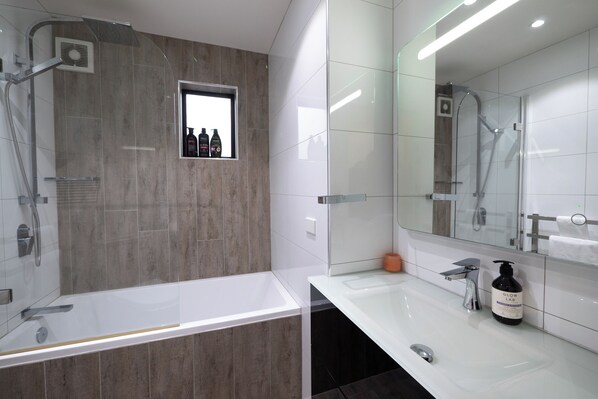 A modern bathroom with a bathtub, shower, and a large mirror.