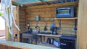 A compact outdoor kitchen with a sink, stove, and microwave, surrounded by wooden walls and a thatched roof. - Cozy campground in beautiful Salobrena with WiFi, AC (Salobrena)