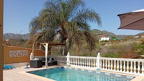 A swimming pool with a pergola and outdoor seating, surrounded by palm trees and a view of hills. - Cozy campground in beautiful Salobrena with WiFi, AC (Salobrena)