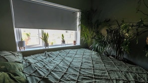 A bedroom with a bed, a window with plants, and a view of the outside. - Stylish & Spacious Family Home On Edge of City (Cork)