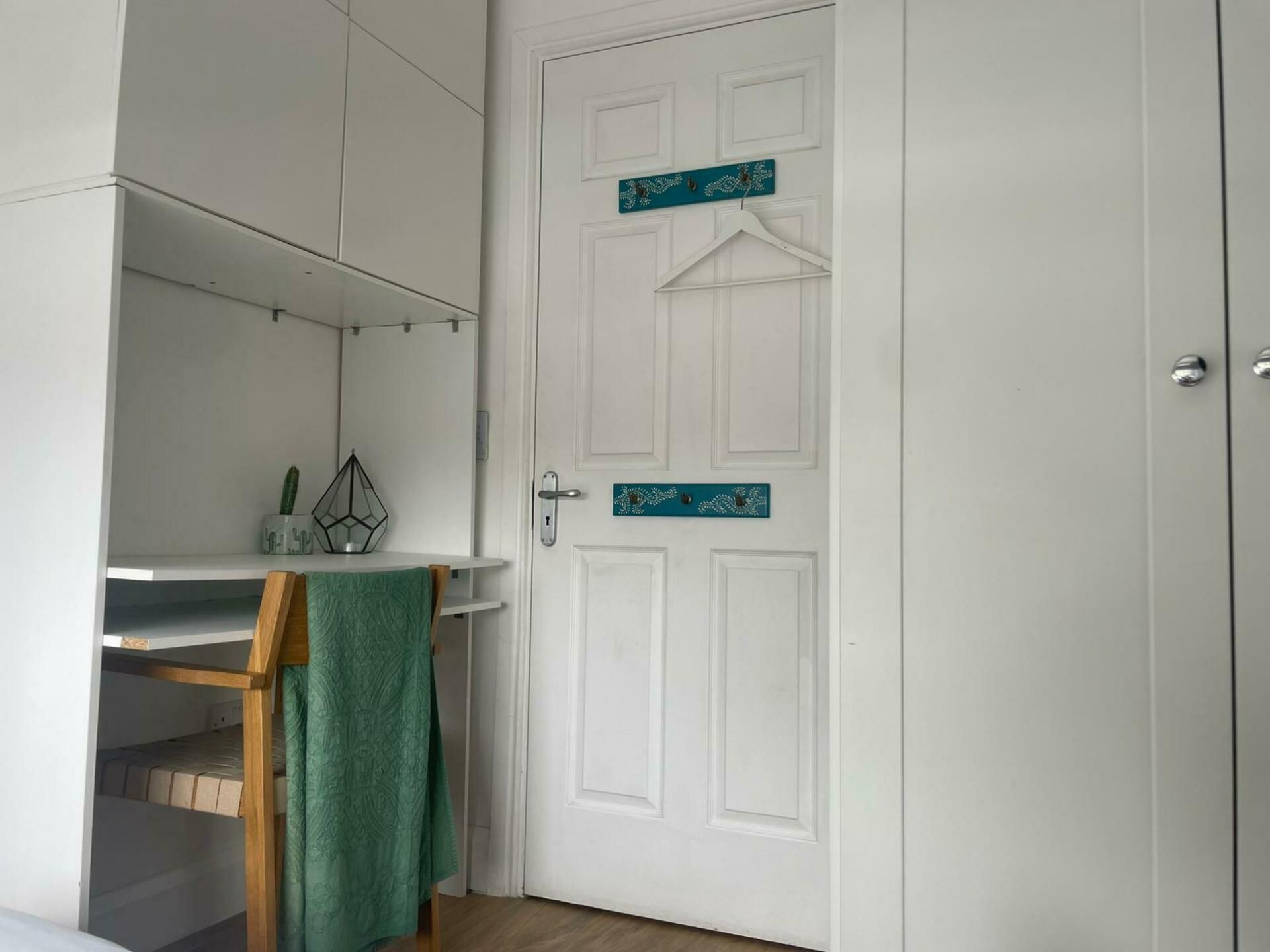 A room with a white door, a small shelf with a hanging garment, and a wooden chair.