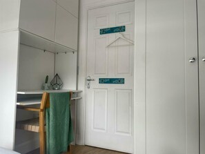 A room with a white door, a small shelf with a hanging garment, and a wooden chair.