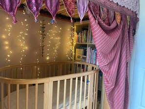 Ein hölzernes Kinderbett mit geschwungener Stange, ein Bücherregal voller Bücher und Lichterketten.