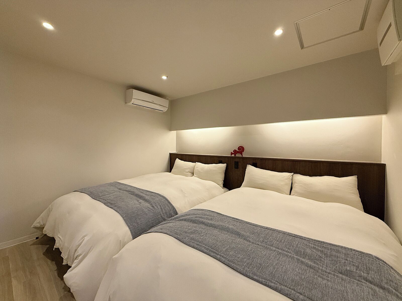 Habitación de hotel con dos camas, cabecero de madera y aire acondicionado instalado en el techo.