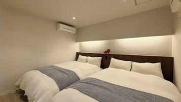 Habitación de hotel con dos camas, cabecero de madera y aire acondicionado instalado en el techo.