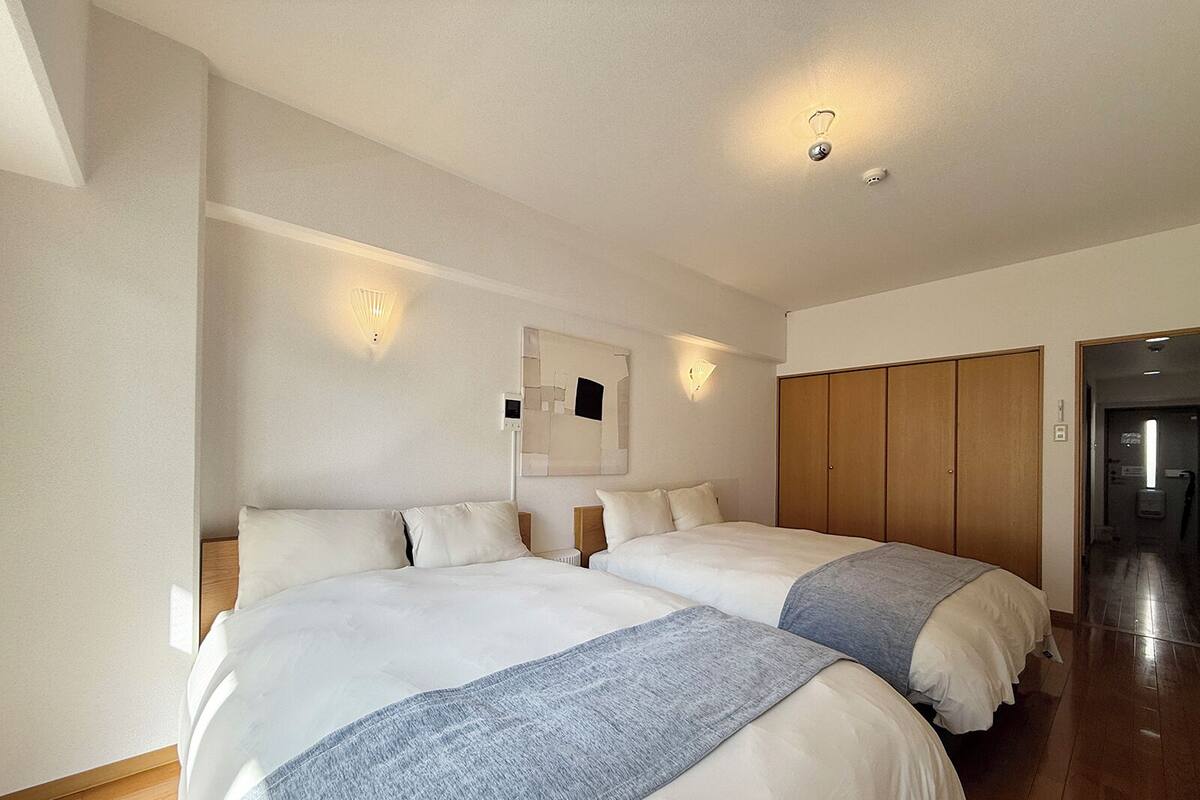 A hotel room with two beds, a wooden wardrobe, a mirror, and wall-mounted lights.