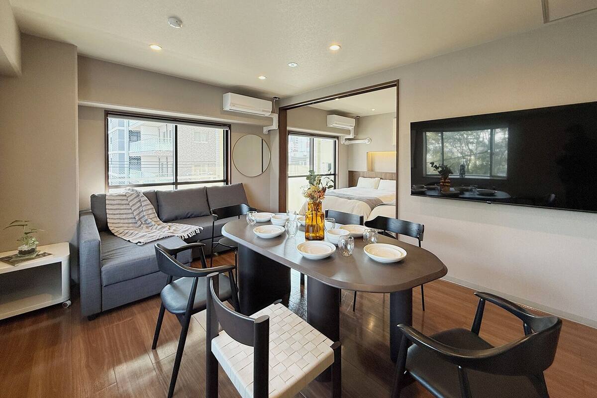 A modern living room with a sofa, dining table, chairs, and a TV.