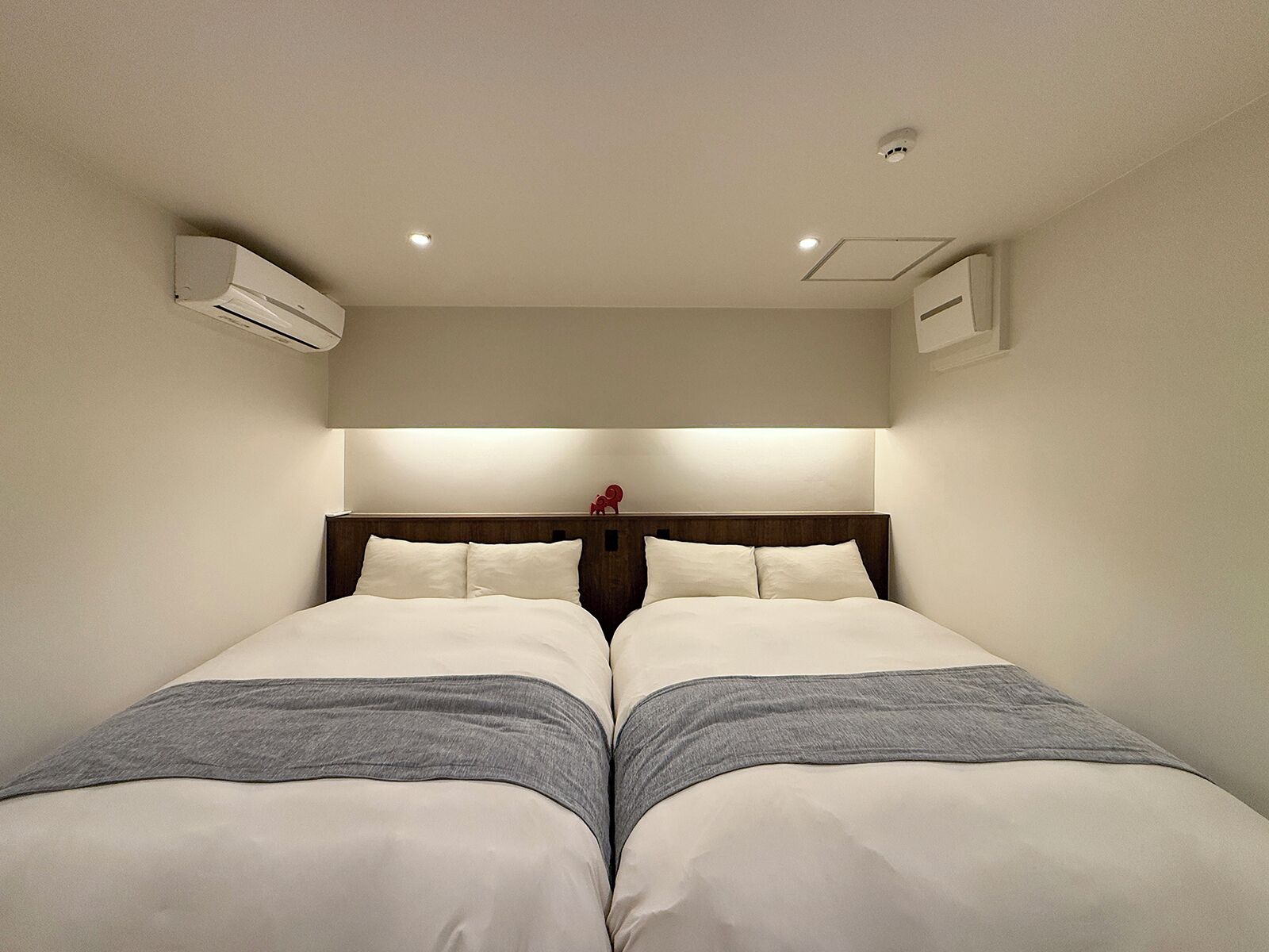 A hotel room with two beds, a wooden headboard, and an air conditioning unit on the wall.