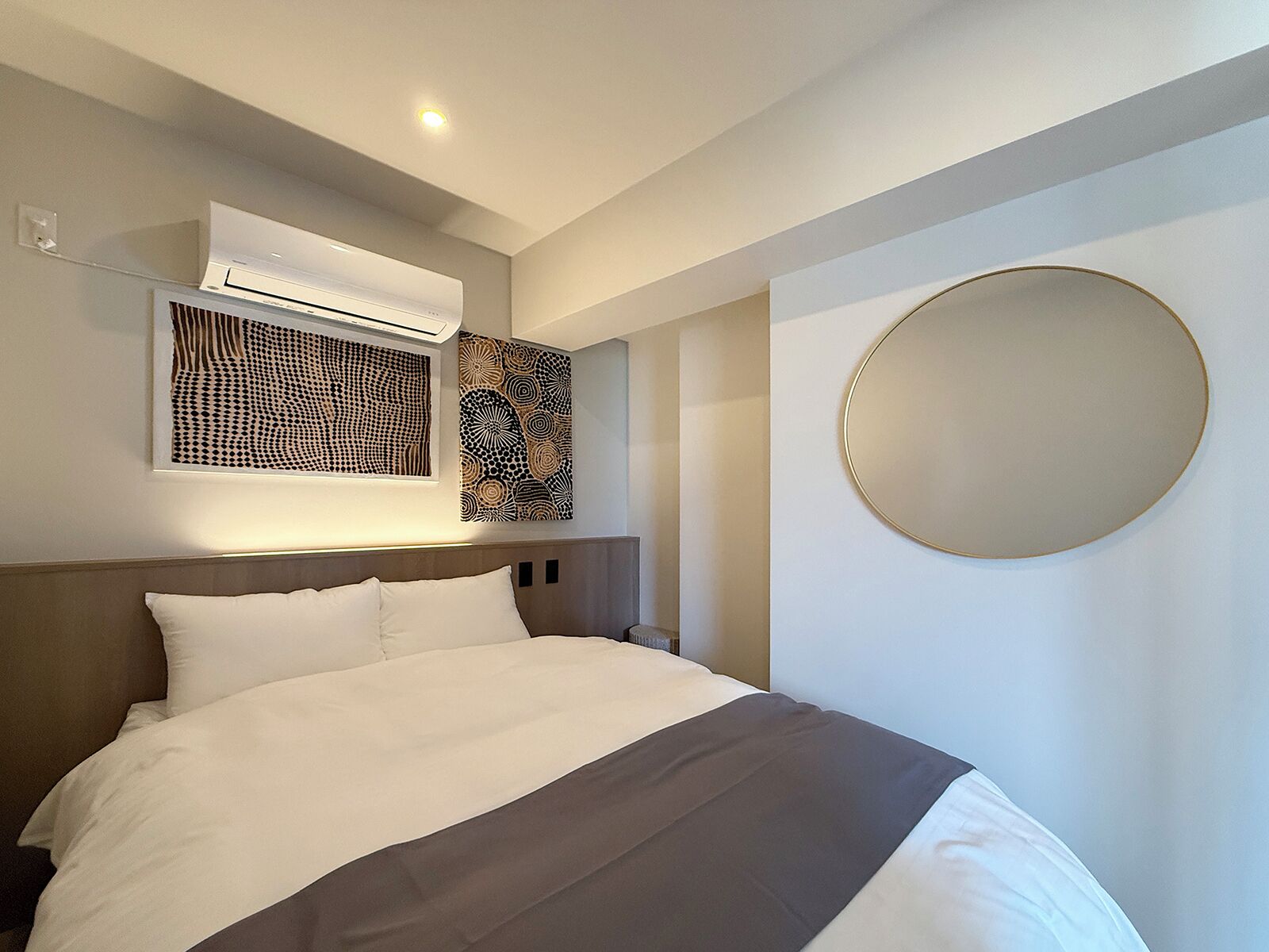Moderni hotellihuone, jossa on suuri sänky, ilmastointilaite ja kaksi abstraktia taideteosta seinillä.