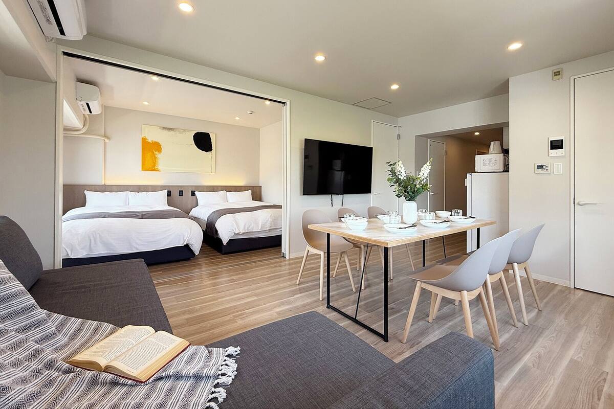 A modern hotel room with a bed, a dining area, and a TV.