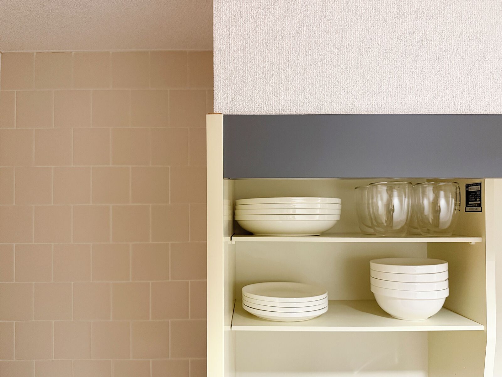 Un meuble de cuisine avec des carreaux beiges sur le mur, des étagères blanches et divers ustensiles de cuisine blancs.