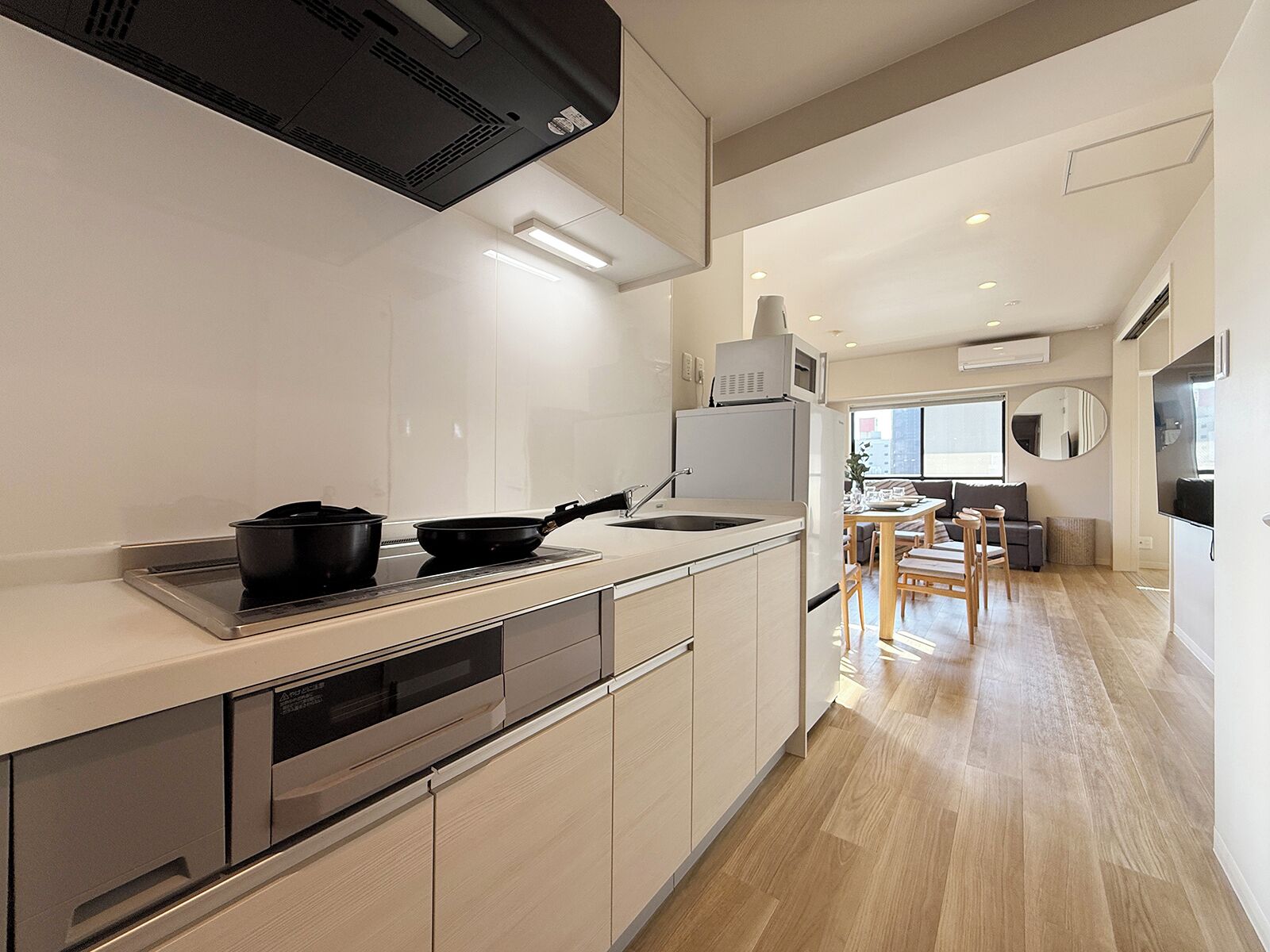 A modern kitchen with a built-in oven, microwave, and dishwasher. There is a dining area with a table and chairs, and a large window providing natural light.
