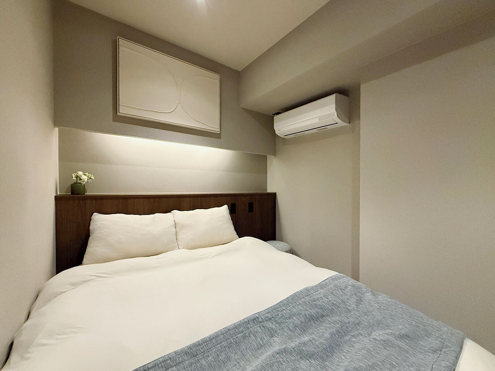 A hotel room with a bed, a wall-mounted air conditioner, and a framed picture above the bed.