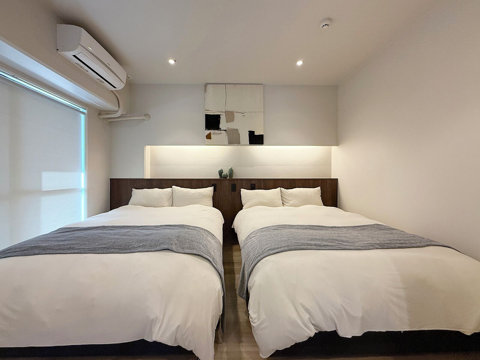 A modern hotel room with two beds, a large mirror, and an air conditioning unit.