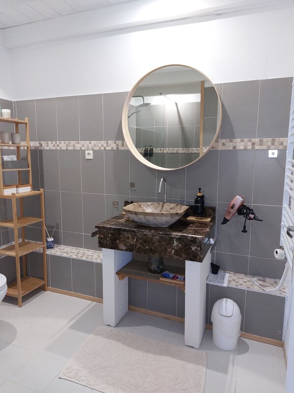 A bathroom with a round mirror, a wooden shelf, a sink, and a hairdryer. - Charming renovated farmhouse with large pool (Lacour)