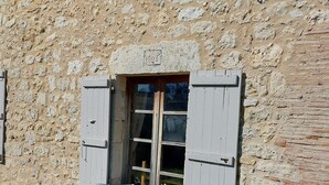A stone building with a window and shutters, a bench outside, and a small window above the door. - Charming renovated farmhouse with large pool (Lacour)