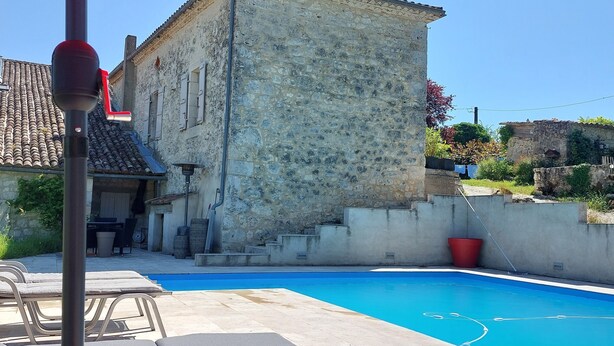 A stone building with a swimming pool, lounge chairs, and a red umbrella. - Charming renovated farmhouse with large pool (Lacour)
