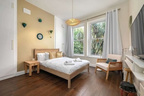 A bedroom with a bed, bedside tables, a chair, a TV, and large windows with curtains.