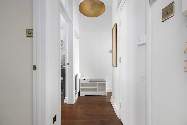 Un pasillo con paredes blancas, suelo de madera, una lámpara colgante y un banco blanco.