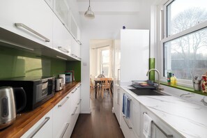 A modern kitchen with white cabinetry, a wooden countertop, and a window with a view of trees.
