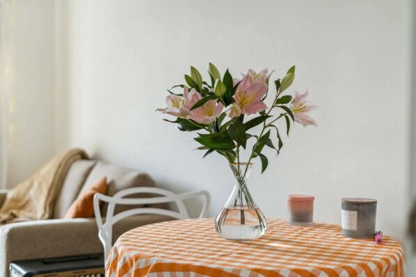 A table with a checkered tablecloth, a vase with pink flowers, and two candles on the table.