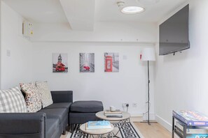 A modern living room with a sofa, a small coffee table, and a flat-screen TV mounted on the wall.