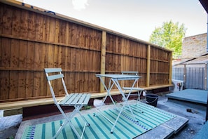 Un espace patio agrémenté d’une clôture en bois, d’une table, de deux chaises et d’un tapis.