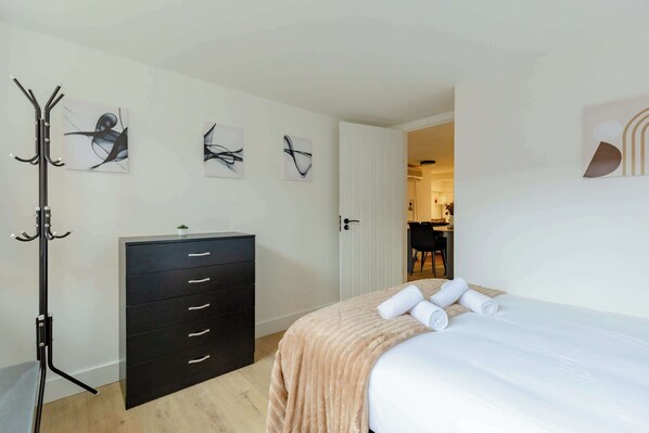 A bedroom with a bed, a dresser, a coat rack, and abstract wall art.