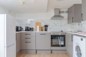 A compact kitchen with a built-in oven, a washing machine, and a coffee maker.