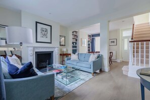 A living room with a fireplace, a sofa, a coffee table, and a bookshelf. - Refined 2BD Flat Between Westminster and Chelsea (Greater London)