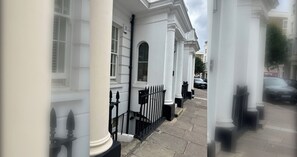 A row of white buildings with black railings and a paved street.