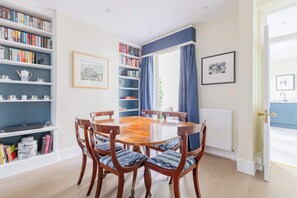 A dining room with a round wooden table, six chairs, and bookshelves filled with books and decorative items.