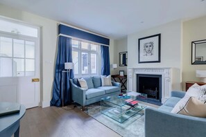 A living room with a sofa, a glass coffee table, a fireplace, and a door.