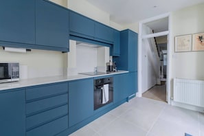 Een moderne keuken met blauwe kastjes, een magnetron en een fornuis.