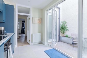Eine moderne Küche mit einem blauen Schrank, einem weißen Heizkörper und einer Glastür, die zu einem Außenbereich mit einer Bank und einem Pflanzgefäß führt.
