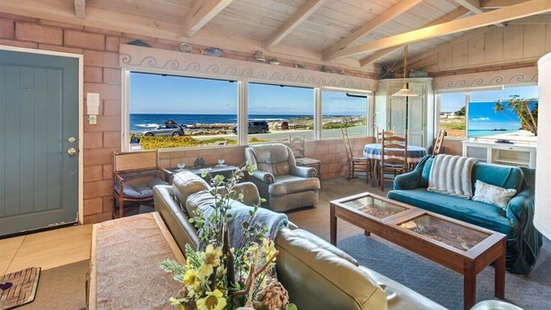 A spacious living room with a large window overlooking the ocean, furnished with leather sofas and a coffee table. - 3976 Beach House on Asilomar~ Oceanfront View Home (Pacific Grove)