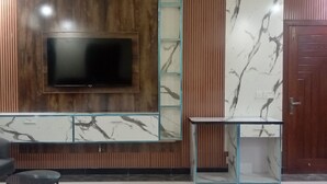 Una sala de estar moderna con un televisor de pantalla plana montado en una pared de madera, una mesa de centro de vidrio y un mueble con diseño de mármol.