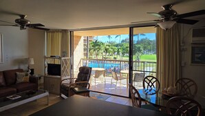 A room with a balcony, a TV, a sofa, and a dining area with chairs and a table.
