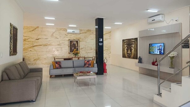 A hotel lobby with a marble wall, a sofa, a coffee table, a TV screen, and a staircase. - Araripina Palace Hotel (Araripina)