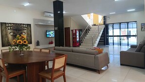 A modern living room with a dining area, a sofa, a TV, and a staircase leading to another level. - Araripina Palace Hotel (Araripina)