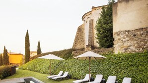 Une piscine entourée d’un mur de pierre et de verdure, avec des chaises longues et des parasols.