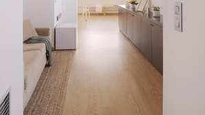 Un intérieur moderne et épuré, avec un plancher en bois, un canapé, un coin repas et une cuisine dotée d’une fenêtre.