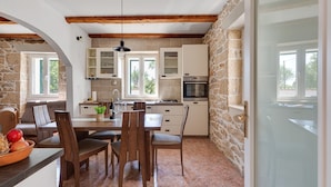 A kitchen with stone walls, wooden beams, and a dining area with a table and chairs. - Haus Zdravko in Prkos  - Haus für 4 Personen (Prkos)