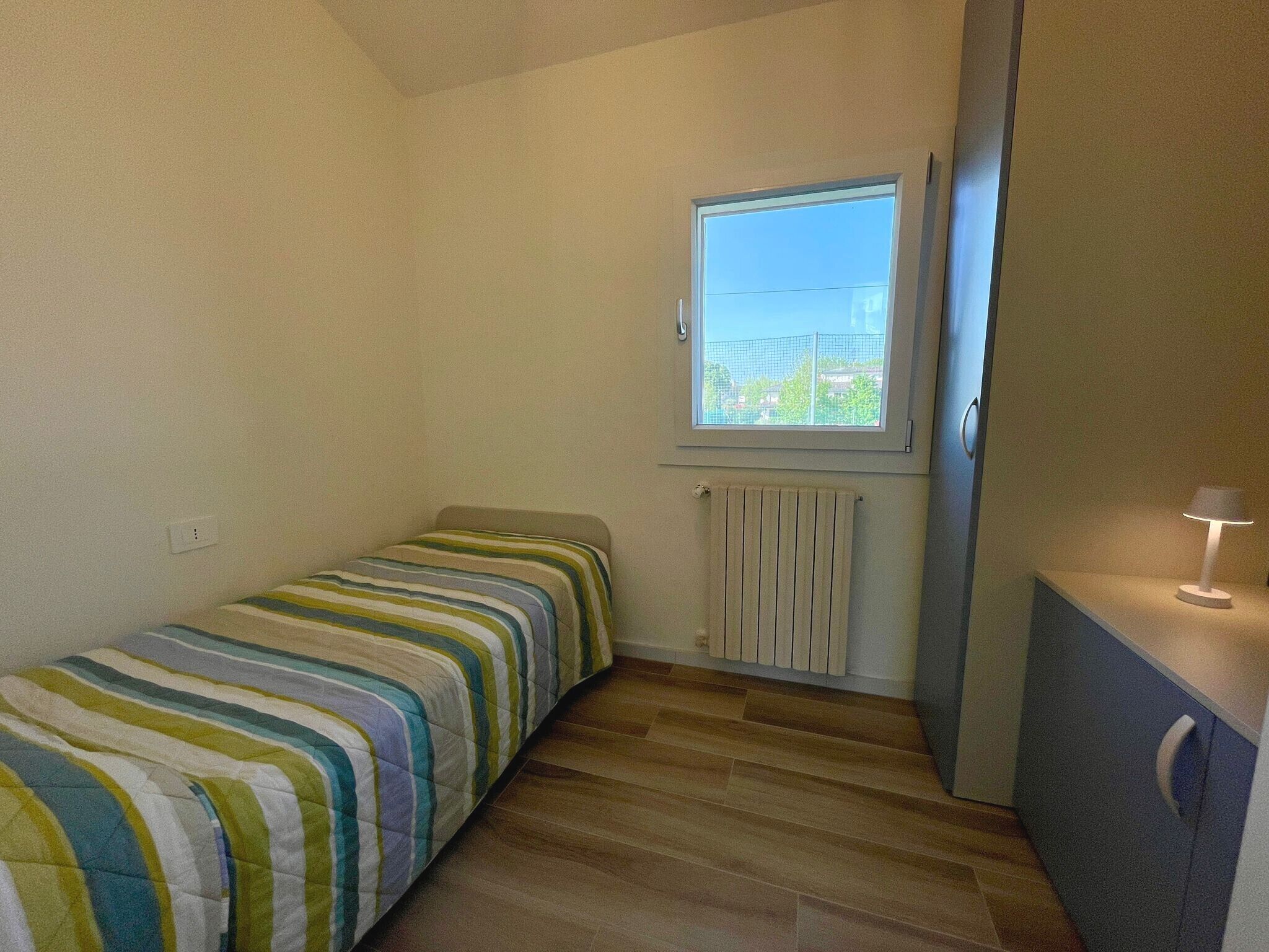 En liten lägenhet med ett rum, bestående av en säng, ett element, ett fönster och ett skrivbord med en lampa.