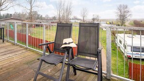 A deck with two chairs and a table, overlooking a fenced yard with a trailer and a playground.