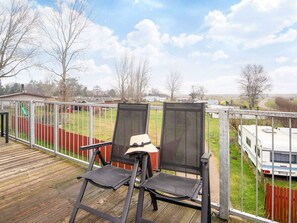 A deck with two chairs and a table, overlooking a fenced yard with a trailer and a playground.