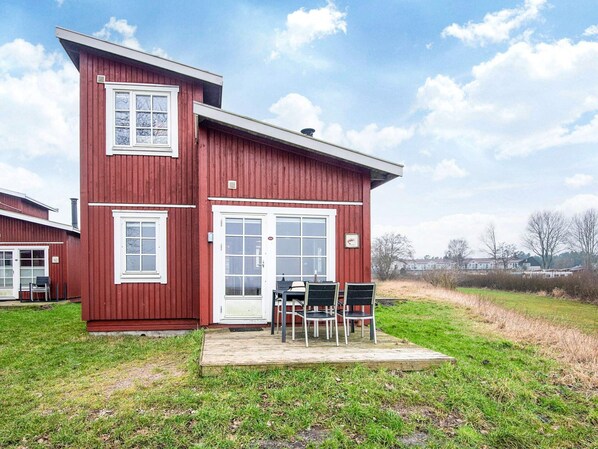 Een rode, twee verdiepingen tellende woning met een voortuin en een kleine tafel en stoelen.