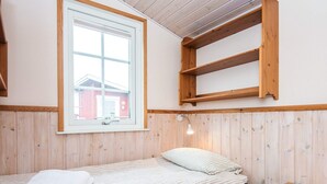 A small, cozy room with a single bed, a wooden table, and a window with a view of a red building outside.
