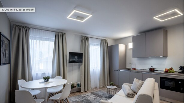A modern living room with a white sofa, a dining table with chairs, and a kitchen area with cabinets and a TV. - Apartment in Schwaz Near Kellerjoch Ski Area (Schwaz)