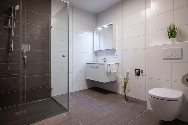 A modern bathroom with a glass shower enclosure, a white toilet, a vanity with a mirror, and a potted plant. - Apartment in Schwaz Near Kellerjoch Ski Area (Schwaz)